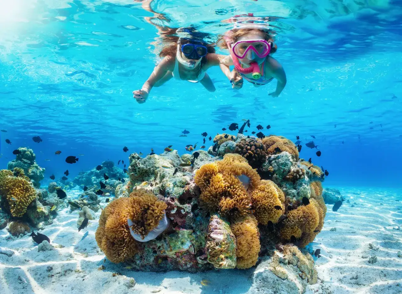 Dzieci w maskach do snorkelingu pływają nad rafą koralową pełną ryb. Niezapomniane wycieczki z Sharm El Sheikh.