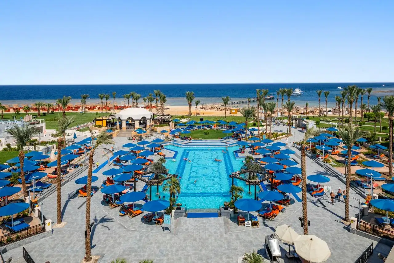 Albatros Palace Port Ghalib: basen, plaża i palmy. Wiele niebieskich parasoli i leżaków zachęca do relaksu.