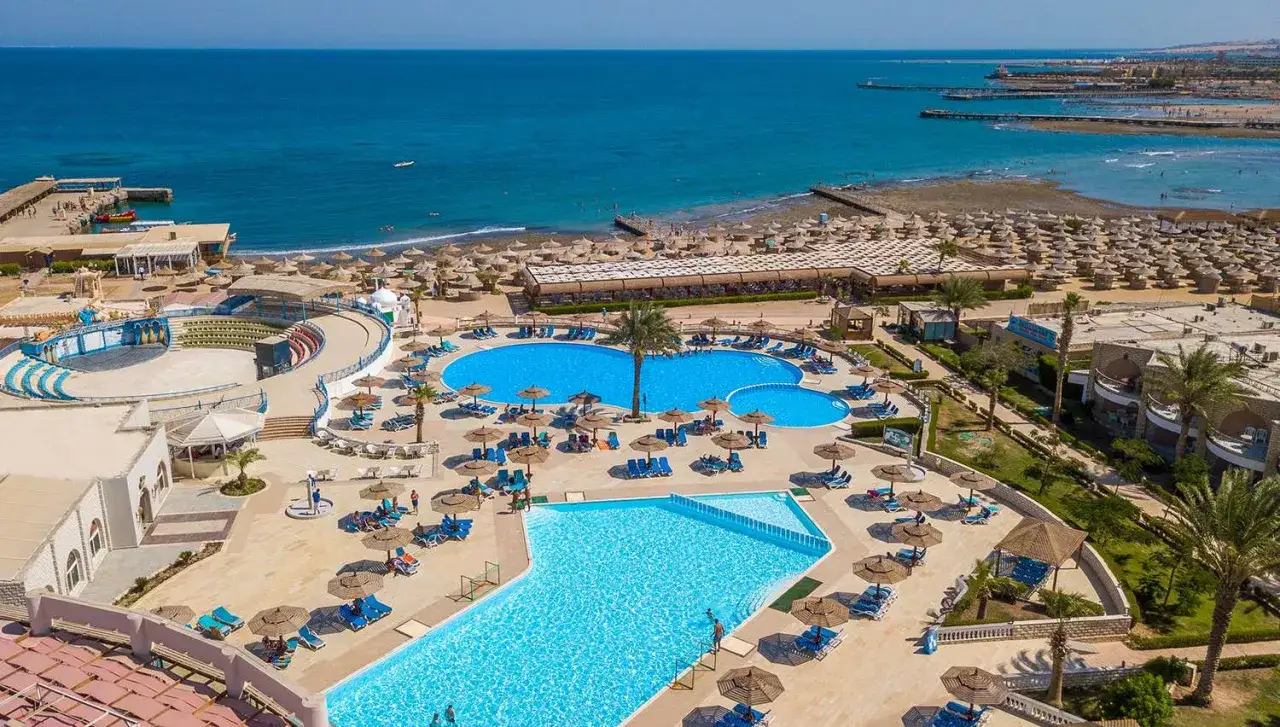 Widok na kompleks basenów i plażę z leżakami. Wiele osób odpoczywa, co potwierdza pozytywne aladdin beach resort opinie.