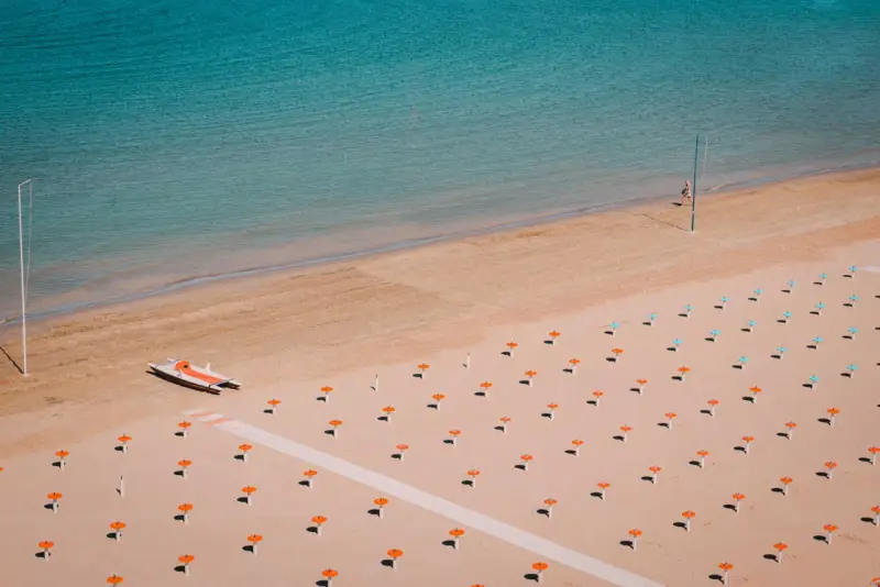 Idealne loty do Rimini: pusta plaża z rzędami parasoli, łódka na piasku i turkusowe morze.